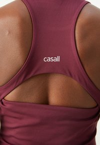 Bordo atletski top s reljefom u obliku ključa na leđima. Mekana tkanina s glatkom teksturom i bijelim "casall" logotipom na leđima.