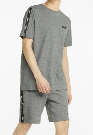 Mann trägt ein graues Puma-Kurzarmshirt und passende Shorts mit schwarzen Puma-Logostreifen an Ärmeln und Seiten.