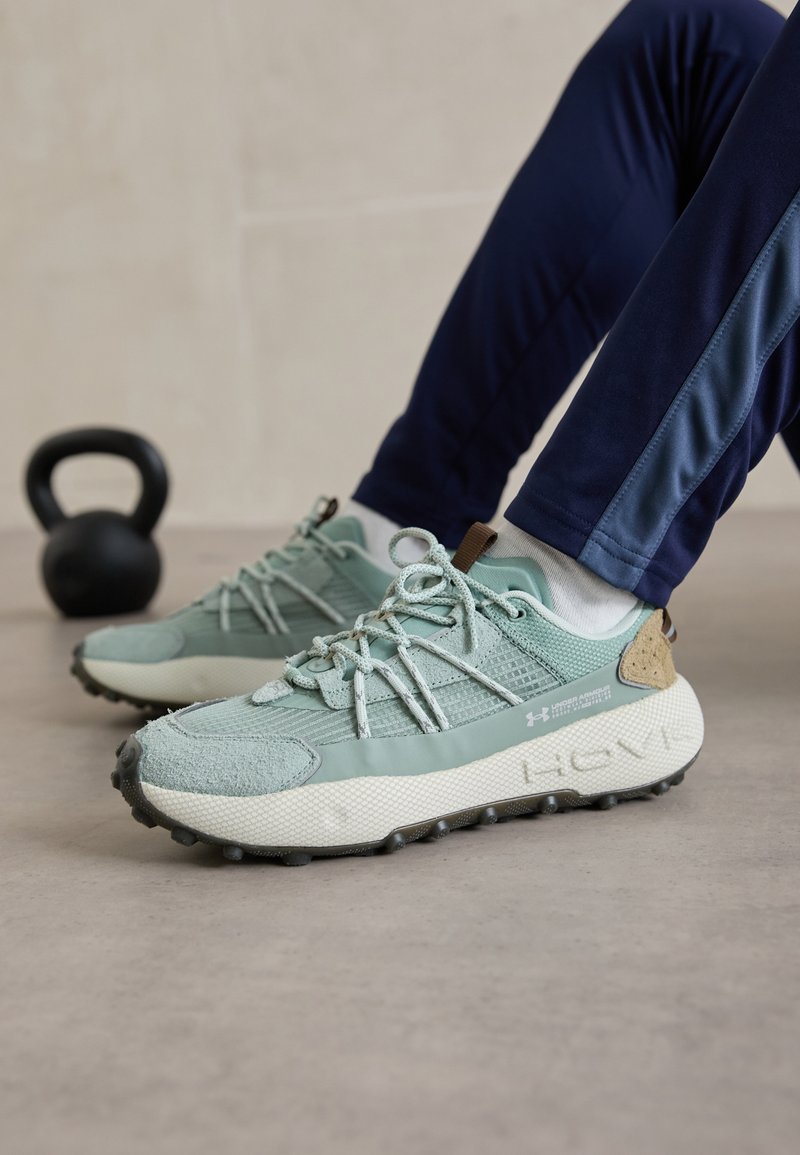 Baskets de sport vert clair avec une tige texturée, un col rembourré et une semelle en caoutchouc ; dotées de lacets flexibles et d'un logo sur le côté.
