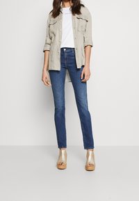 Ljusbeige linneskjorta med uppkavlade ärmar, vit t-shirt med logotyp, mörkblå slim fit-jeans och beige öppen tå plattformsskor.