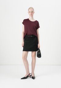 Bordeaux kortermet topp, svart tettsittende skjørt med beltehemper, kombinert med svarte slingback-hæler og en liten teksturert håndveske.
