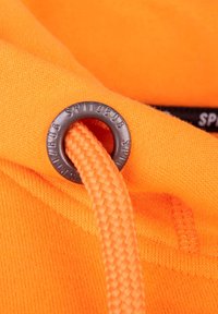 Oranje hoodie met een gevlochten koord door een zwart metalen oogje, met een gladde stoftextuur en contrasterende zwarte logodetail.