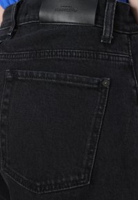 Jeans in denim nero con una tasca posteriore con cuciture tonalità e una patch in pelle nera del marchio appena sopra. Forma classica e tessuto testurizzato.