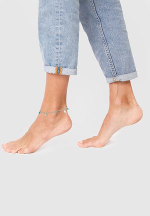 Sølv ankelarmbånd med små turkis perler, båret om en ankel, parret med oprullede lyseblå jeans. Trædetaljer synlige på jeansene.
