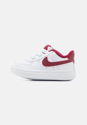 Baskets blanches pour tout-petit avec le swoosh rouge Nike et un col rembourré rouge sur fond blanc.