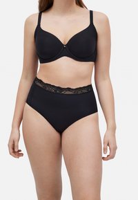 Sujetador negro con copas lisas y tirantes ajustables, combinado con braguitas negras de talle alto con una cinturilla de encaje.