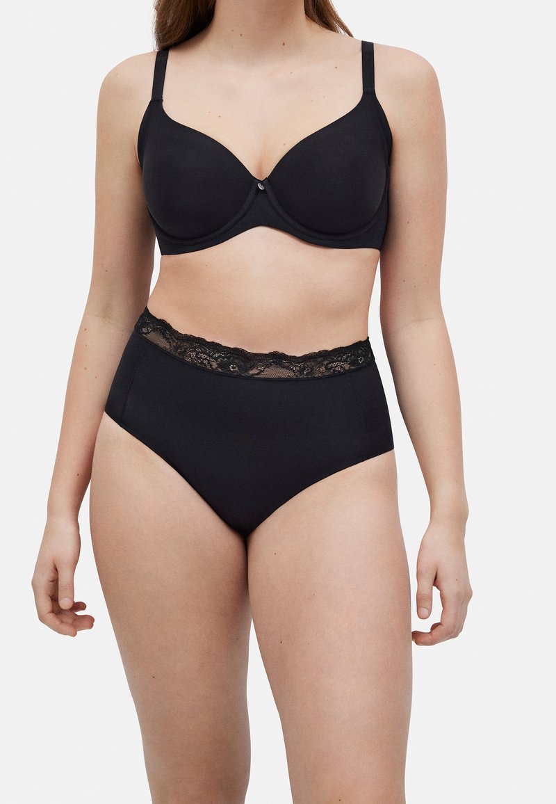 Sujetador negro con copas lisas y tirantes ajustables, combinado con braguitas negras de talle alto con una cinturilla de encaje.