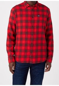 Chemise flanelle à carreaux rouges et noirs avec un col button-down, des manches longues et un petit logo sur la poche poitrine gauche.