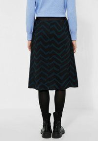Černá sukně s tyrkysovým zigzag vzorem, ke kolenům, s elastickým pasem, kombinovaná s černými punčochami a kotníkovými botami. Hladká textilie.