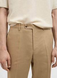 Pantalones beige ajustados con frente plano, trabillas para cinturón y cierre de botón único. Tela ligera con una textura suave.