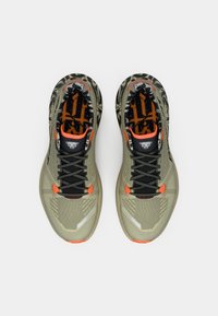 Παπούτσια για τρέξιμο σε μονοπάτια με ελαφρύ ελιά χρώμα στο επάνω μέρος, μαύρους κορδόνες, πορτοκαλί λεπτομέρειες, και σχέδιο στην εσωτερική επένδυση. Υφή με ανακλαστικές λεπτομέρειες.