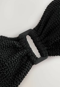 Svart elastisk band med en texturerad, veckad design och en slät, matt rektangulär spänne i mitten.