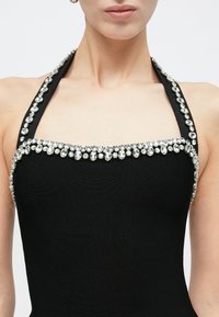 Μαύρο φόρεμα με λαιμόκοψη halter από υφή ύφασμα, διακοσμημένο με διάφανα στρας κατά μήκος του ντεκολτέ και των ιμάντων στους ώμους.