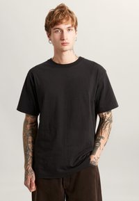 Black cotton t-shirt with a crew neckline and short sleeves, featuring a smooth texture and a relaxed fit. Minimalist design, no patterns.