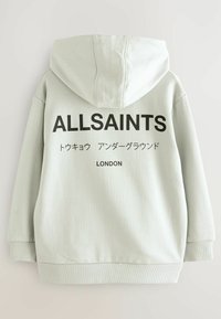 Sudadera con capucha verde claro con un gran logo negro "ALLSAINTS" en la parte trasera, que incluye texto en japonés y la palabra "LONDON" debajo. Tela suave y puños acanalados.