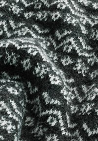 Plaid en tricot présentant un motif en zigzag en gris foncé et blanc. Surface douce et texturée avec une finition duveteuse et des fibres visibles sur l'ensemble.