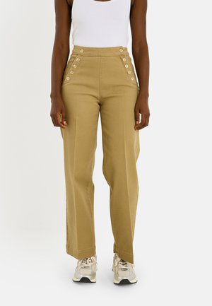 Personne portant un pantalon kaki taille haute avec des boutons décoratifs et des baskets blanches, associé à un haut blanc sans manches.