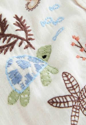 Broderi på hvidt stof med en blå og grøn skildpadde, brune blade og små orange blomster.