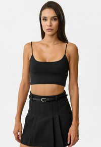 Zwart cropped tanktop met dunne bandjes, gemaakt van glad materiaal, gecombineerd met een zwarte hoogge رتste plissérok en een zwarte riem.