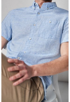 Hellblaues kurzärmeliges Hemd mit Knopfleiste und einer Brusttasche, aus strukturiertem Stoff gefertigt, mit kontrastierenden Nähten und weißen Knöpfen.