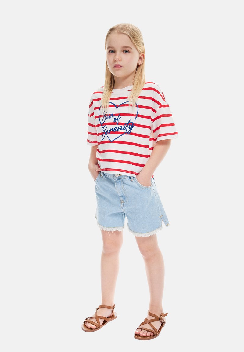 Camiseta a rayas rojas y blancas con gráfico de corazón azul, combinada con pantalones cortos de mezclilla azul claros con bordes deshilachados y sandalias marrones de tiras.