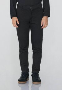 Černé slim-fit kalhoty s knoflíkovým zap�ínáním a pěti kapsami, doplněné černými teniskami s texturovaným povrchem a gumovými podrážkami.