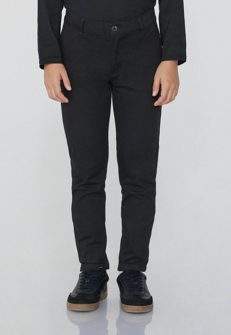 Černé slim-fit kalhoty s knoflíkovým zapínáním a pěti kapsami, doplněné černými teniskami s texturovaným povrchem a gumovými podrážkami.