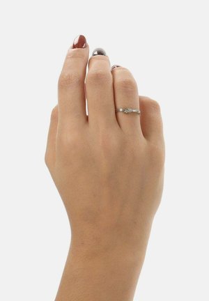 Srebrna obrączka z oplecionym wzorem opaski, z małym węzłowym akcentem. Dłoń z neutralnym lakierem do paznokci pokazuje dopasowanie i szczegóły pierścionka.