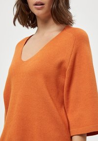 Oranges Strickpullover mit V-Ausschnitt und kurzen, weiten Ärmeln. Weiche Textur mit entspannter Passform, die ein nahtloses Design aufweist.