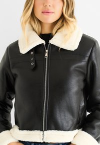 Black leather cropped jacket with a cream faux shearling collar, front zipper closure, and side pockets. Smooth texture with contrasting accents.