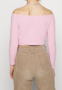 Růžový, texturovaný, top bez ramínek s dlouhými rukávy, spojený se světlými kordovými kalhotami s vysokým pasem, které mají zadní kapsy.