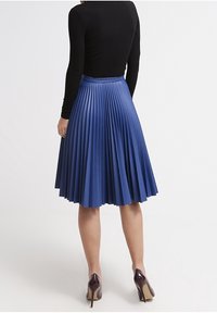 Fållad midiklänning i rik blå färg, tillverkad av slät tyg. Har ett figursytt midjeband och flödande, lager av rynkor. Klackar ger kontrast.