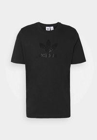 Černé bavlněné tričko s kulatým výstřihem, zdobené texturovaným logem v tečkovaném vzoru. Krátké rukávy a rovný lem.