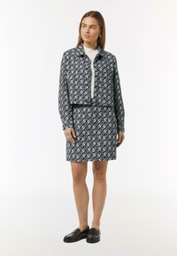 Schwarz-weiß gemusterte, kurze Jacke und passender Rock, beide mit einem filigranen Design; Modell trägt schwarze Slipper.