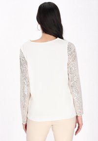 Maglietta a manica lunga con corpo crema e maniche decorate con paillettes lucide, caratterizzata da un colletto rotondo e una texture di tessuto liscia.