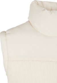 Doudoune sans manches couleur crème avec col montant et panneau en tissu côtelé en bas, conçue pour la chaleur et un usage décontracté.