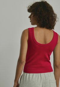 Tætsiddende ribbet tanktop i klar rød med rund hals og cropped design, parret med lysegrå sweatpants.