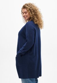 Cardigan bleu marine en tissu texturé, offrant une coupe décontractée, des manches longues et des poches latérales, avec un ourlet et des poignets côtelés.