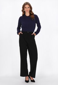 Granatowy sweter ze splotem warkoczowym z koralikowymi akcentami, zestawiony z czarnymi spodniami o wysokim stanem i szerokimi nogawkami oraz czarnymi szpilkami.