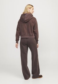 Tmavě hnědý zkrácený hoodie s kapucí a sníženými rameny, doplněný o široké kalhoty ve stejné barvě. Měkká látka s uvolněným střihem.