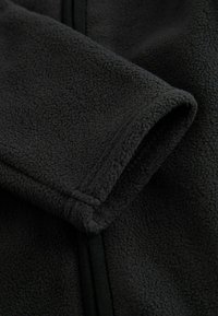 Černá fleecová tkanina s jemnou texturou. Obsahuje hladký zip a šité švy, což ukazuje jednoduchý a praktický design.