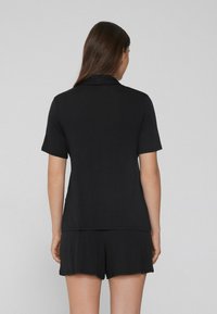 Black short-sleeve polo shirt with a relaxed fit, made from soft fabric. Features a classic collar and a straight hem.