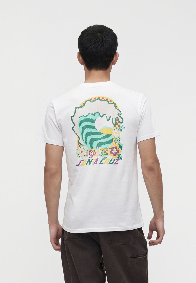 Άνδρας που φοράει λευκό T-shirt με πολύχρωμο γραφικό από στυλιζαρισμένο ωκεάνιο κύμα, ήλιο, λουλούδια, σύμβολο ειρήνης και κείμενο "Santa Cruz" στο πίσω μέρος.