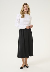 Valkoinen smokkikuvioinen paita pitkillä hihoilla, yhdistetty mustaan, liehuvaan midi-hameeseen. Asusteessa on yksinkertainen, elegantti muotoilu ja tekstuurit.