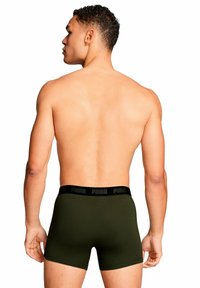 Boxer da uomo PUMA in verde oliva con elastico nero in vita riportante il nome del marchio. Tessuto liscio e design aderente.