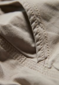 Primo piano di un tessuto beige che mostra dettagli di cucitura, una consistenza liscia e pieghe curve, enfatizzando la leggerezza e la morbidezza del materiale.