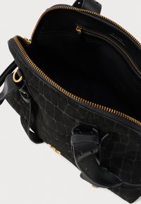 Μαύρη δερμάτινη τσάντα με υφή, με χρυσό φερμουάρ ανοικτό μερικώς, μαύρους δερμάτινους χειρολαβές και ορατή εσωτερική τσέπη με φερμουάρ.