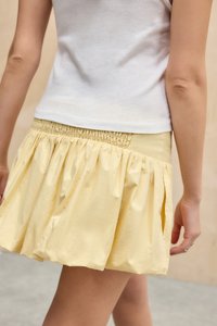 Yellow, textured mini skirt with a gathered, smocked waistband and a flared silhouette, paired with a white fitted top.
