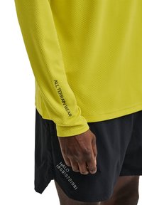 Koszulka z długim rękawem w jasnym żółtym kolorze z siateczkowego materiału o teksturowanej powierzchni. Posiada napis "ALL TERRAIN WEAR" na rękawie oraz czarne szorty.