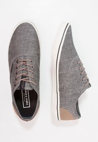 Zapatillas casuales grises hechas de tela texturada con acentos marrones, puntera redonda, suela de goma blanca y diseño clásico de cordones.